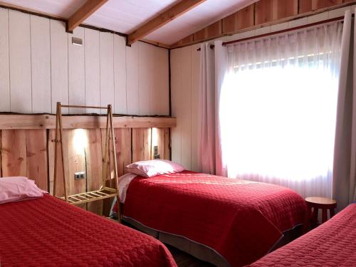 a bedroom with two beds with red sheets and a window at Cabañas Peumayén Neltume in Neltume