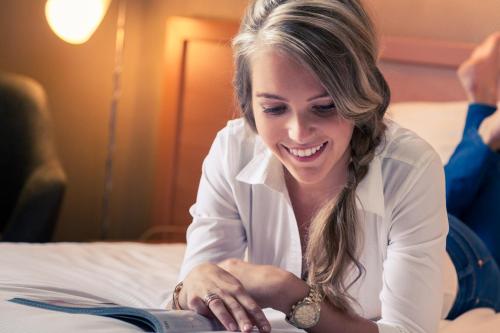 a woman sitting on a bed using a laptop at Mercure Hotel Zwolle in Zwolle