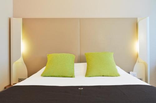 a bedroom with a bed with two lime green pillows at Campanile Villejust - za Courtaboeuf in Villejust