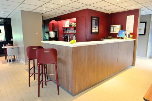 a bar in a restaurant with red walls and stools at Campanile Villejust - za Courtaboeuf in Villejust