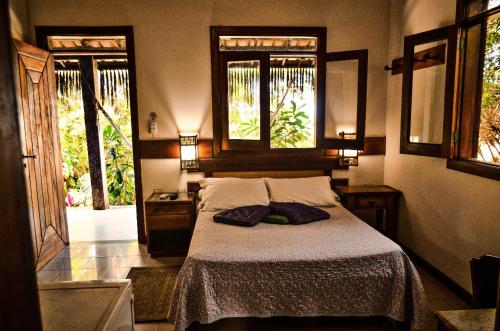 a bedroom with a bed with two pillows and two windows at Pousada Morro dos Navegantes in Ilhéus