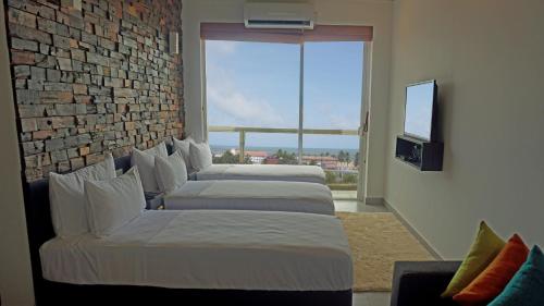 three beds in a room with a large window at Hotel Sico in Negombo