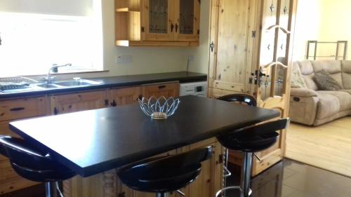 uma cozinha com bancada preta e bancos de bar em Teach Nellie Cottage em Loughanure