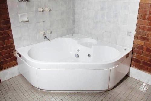 y baño de azulejos blancos con bañera blanca. en Fountain Court Motor Inn Albury en Albury