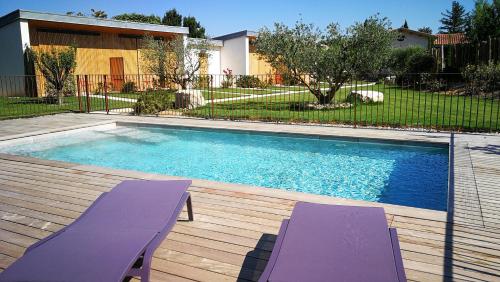 - une piscine bordée de 2 chaises longues violettes dans l'établissement Maison d'hôtes Le Pré Gourmand - Adults only, à Eyragues