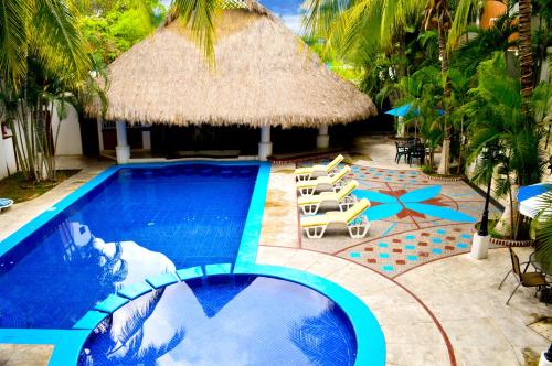 a swimming pool with chairs and a straw umbrella at Hotel Costa Brava in Manzanillo