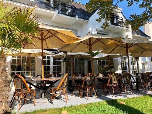 uma área de refeições exterior com mesas, cadeiras e guarda-sóis em Hôtel-Restaurant La Mascotte em La Baule