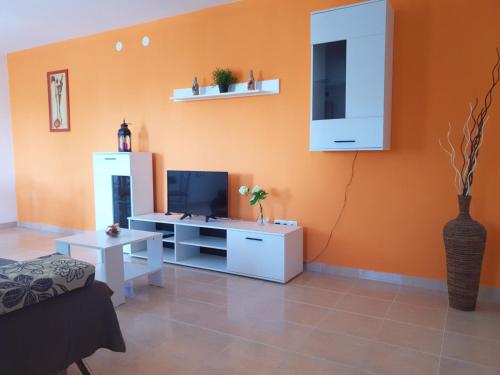 sala de estar con pared de color naranja y TV en Apartmani "Bodulo" en Povljana