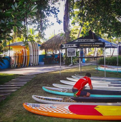 a man sitting on a row of surfboards on the grass at Beach Break Resort & CR Surf Camp in Jacó