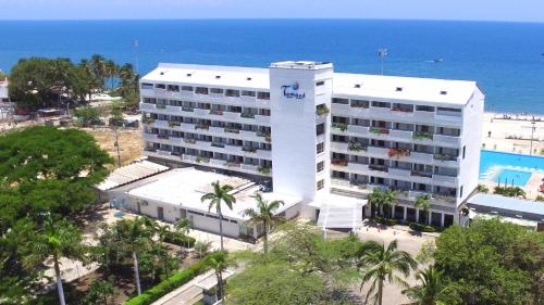 a large white hotel with the ocean in the background at Tamaca Beach Resort in Santa Marta