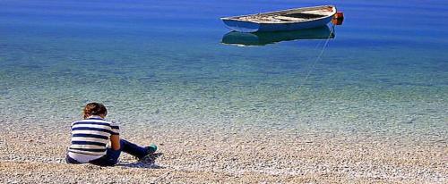 Un niño sentado en la playa viendo un barco en el agua en Apartment Marija, en Split