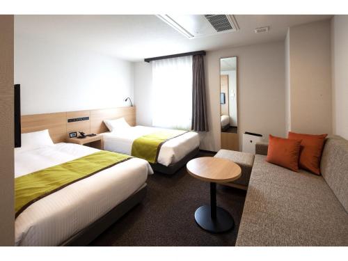 Y's Hotel Asahikawa Ekimae في اساهيكاو: غرفة فندقية بسريرين واريكة