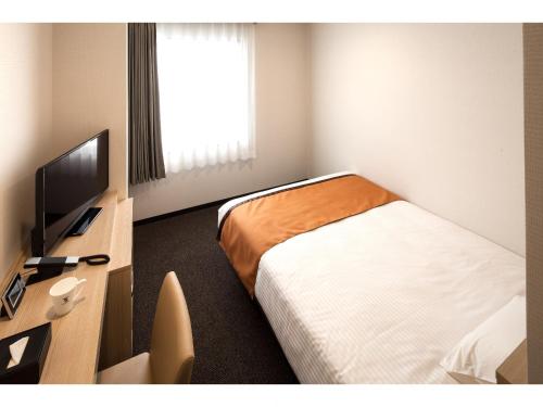 a hotel room with a bed and a desk with a television at Y's Hotel Asahikawa Ekimae in Asahikawa