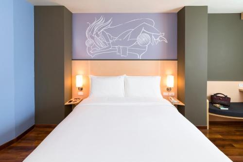 a bedroom with a large white bed with a drawing on the wall at ibis Vientiane Nam Phu in Vientiane