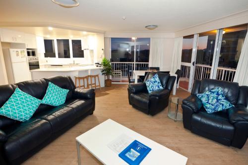 a living room with black leather furniture and a kitchen at Meridian Tower Kirra Beach in Gold Coast