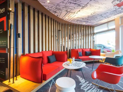 a room with a red couch and chairs and tables at ibis Deauville Centre in Deauville