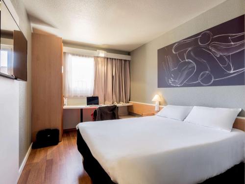a hotel room with a large white bed and a desk at Ibis Granada in Granada