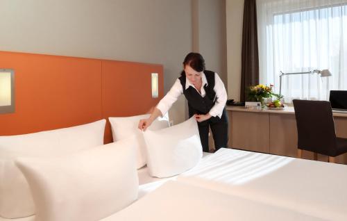 a woman in a hotel room putting pillows on a bed at Essential by Dorint Berlin-Adlershof in Berlin