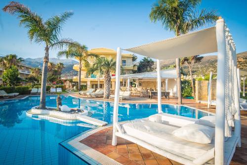 a resort pool with a bed and palm trees at Parthenis Hotel & Suites in Malia