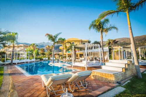 a resort swimming pool with chairs and palm trees at Parthenis Hotel & Suites in Malia