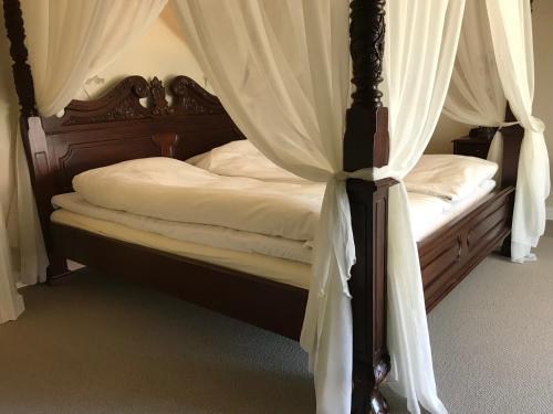 a bed with a canopy with white sheets and curtains at Bramslevgaard in Hobro