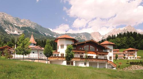 ein Gebäude auf einem Hügel mit Bergen im Hintergrund in der Unterkunft Hotel Leitenhof 4 Sterne Superior in Scheffau am Wilden Kaiser