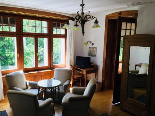 ein Wohnzimmer mit Stühlen, einem Tisch und Fenstern in der Unterkunft Stilvolle 3-Zimmer Wohnung in Jugendstilvilla in Flims