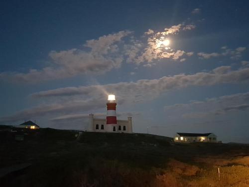 a lighthouse on a hill with the moon in the sky at Beachcombers in Agulhas