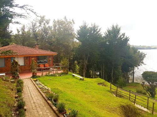 a house on a grassy hill next to the water at Cabañas Yukatan Lago de Tota in Tota