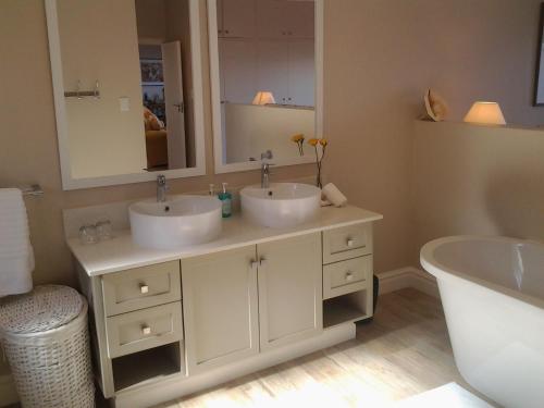 een badkamer met 2 wastafels, een bad en een spiegel bij Our Beach House in Southbroom
