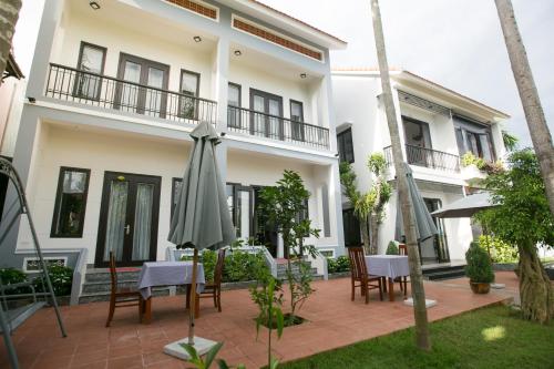 a patio in front of a white building with an umbrella at Yen villa Hội An in Hoi An