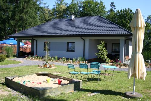 a house with chairs and an umbrella and a sandbox at Domki przy Dworskiej in Polańczyk