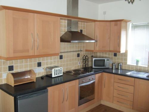 une cuisine avec des placards en bois et un comptoir noir dans l'établissement Aird Cottage, à Aird