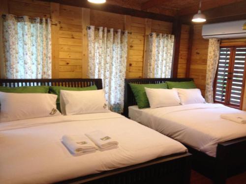 two beds in a room with wooden walls and windows at Nung Ni Bang Khon Thi Resort in Amphawa