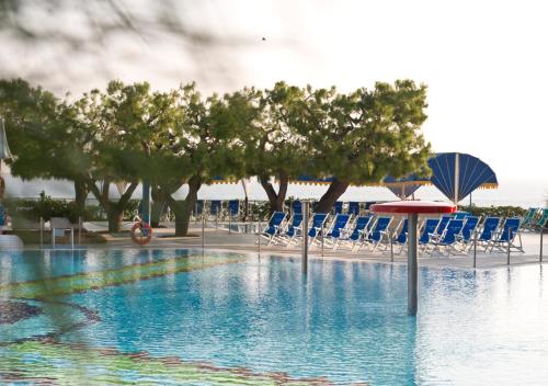 a swimming pool with chairs and umbrellas and trees at Corvino Resort in Monopoli