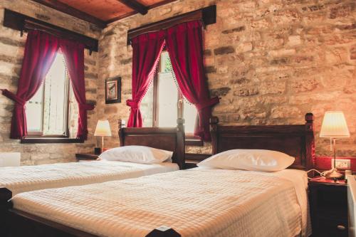 two beds in a bedroom with red curtains at Hotel Kastro in Gjirokastër