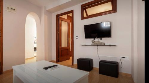 sala de estar con mesa y TV en la pared en APARTAMENTOS HÉRCULES SEVILLa, en Sevilla