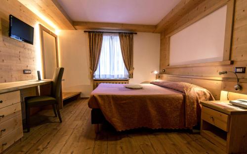 a bedroom with a bed and a desk and a window at Hotel Siera Hof in Sappada