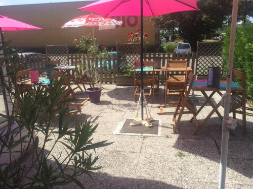 a patio with tables and chairs and a pink umbrella at Hôtel Inn Design Resto Novo Amiens in Dury
