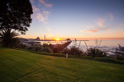 a sunset over a body of water with a grass field at Belt Road Seaside Holiday Park in New Plymouth