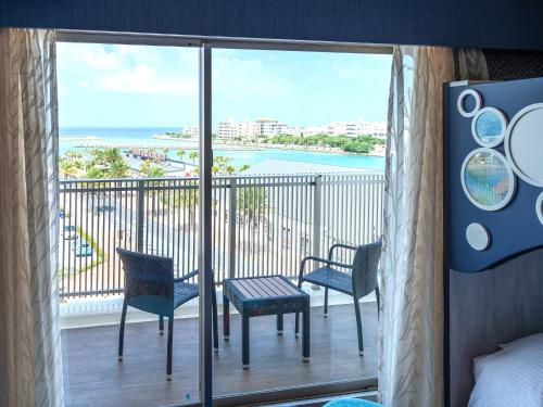 a room with a balcony with chairs and a view of the ocean at La'gent Hotel Okinawa Chatan Hotel and Hostel in Chatan