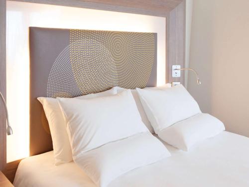 a bed with white pillows in a bedroom at Novotel Paris Nord Expo Aulnay in Aulnay-sous-Bois