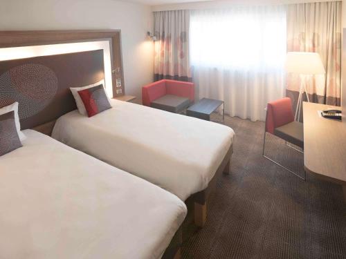 a hotel room with two beds and a desk at Novotel Paris Nord Expo Aulnay in Aulnay-sous-Bois