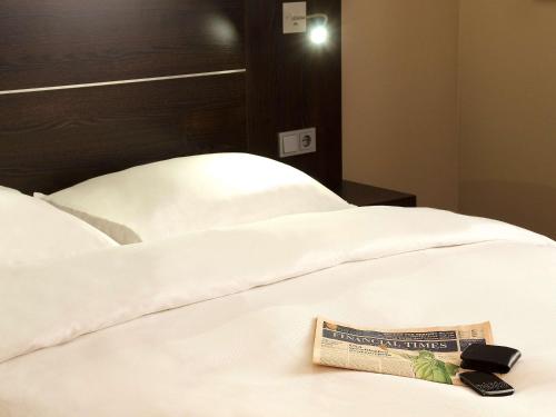 a book on a bed with a remote control on it at Mercure Hotel Hagen in Hagen