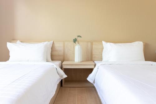 two beds with white sheets and a vase on a table at O2 Hotel Lopburi in Lop Buri