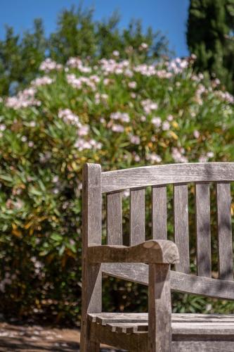 a wooden bench in front of a bush with pink flowers at Hotel Cala di l'Oru in LʼÎle-Rousse