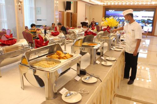 a chef standing in front of a buffet line with food at Fu Hua International Hotel Dunhuang in Dunhuang