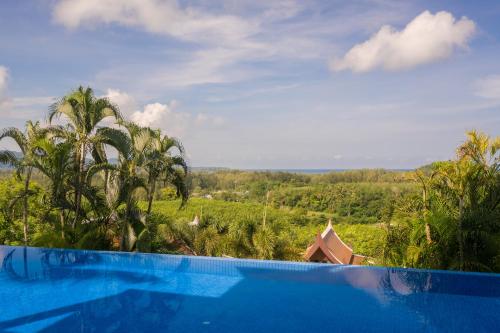 a blue swimming pool with a view of a forest at Vichuda Hills by RESAVA in Layan Beach