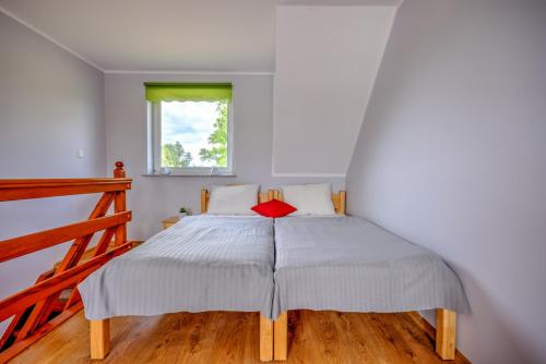 a white bedroom with a bed with a red pillow at Domki przy zalewie in Kamień Pomorski