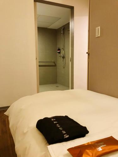 a black shirt sitting on a bed with a shower at Single Inn-Kaohsiung Station in Kaohsiung